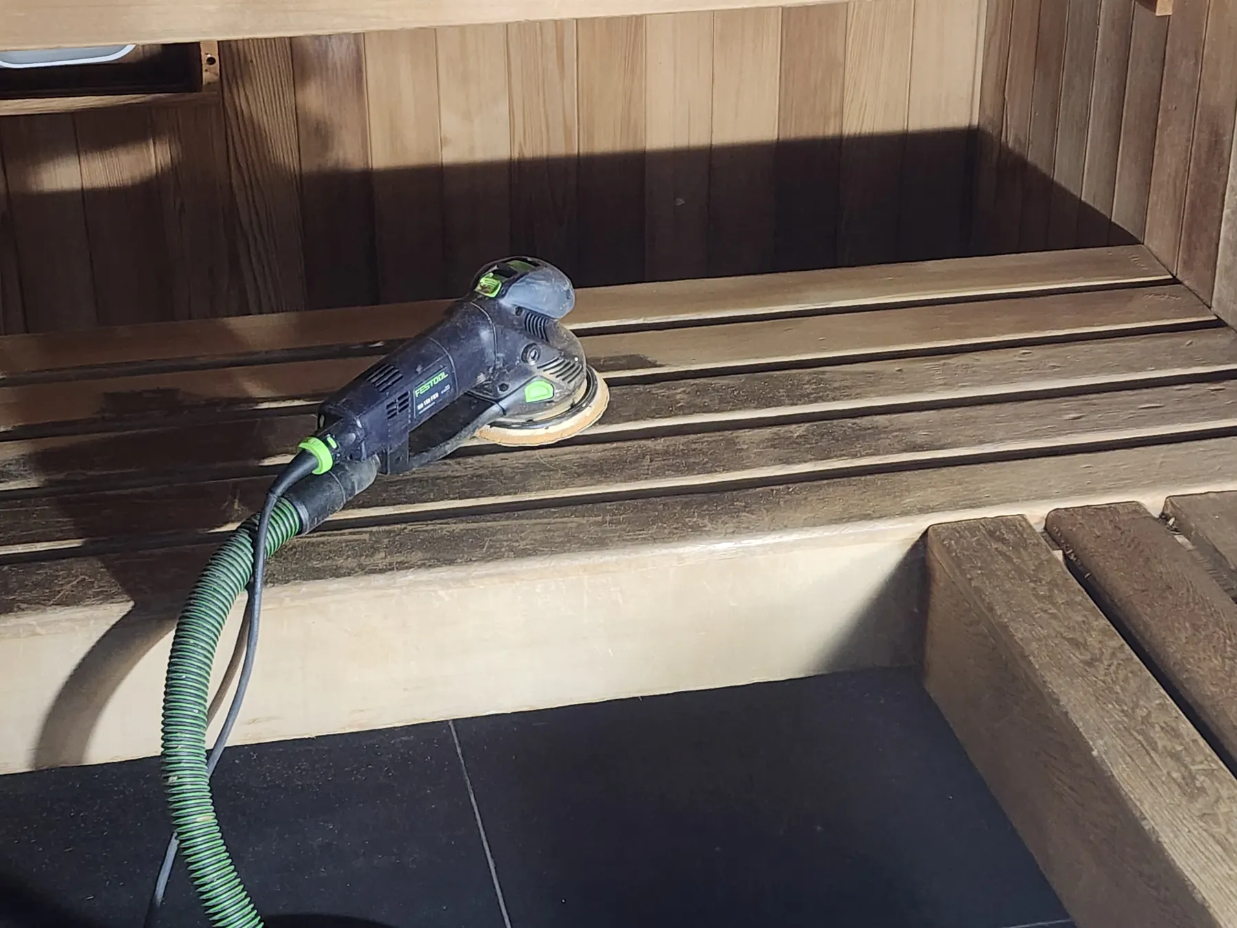 Sanding the sauna benches with a random orbital sander
